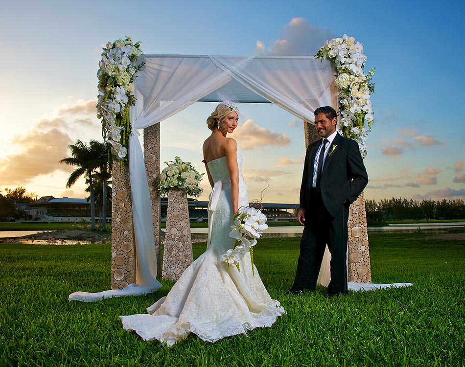 Photo of a bride and groom standing in front of an arch on the lawn